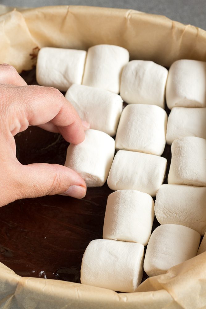 hand placing marshmallows on top of chocolate layer in square baking dish
