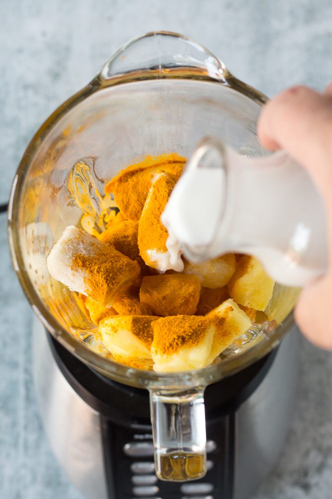 pouring almond milk in blender to make pineapple turmeric tahini shake by Flora & Vino
