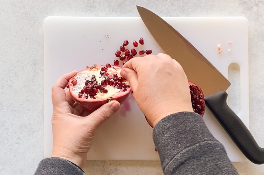 seeding pomegranate on a cutting board with a knife by Flora & Vino