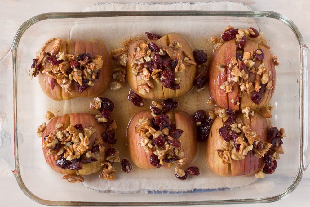 Hasselback Baked Apples topped with nuts and seeds in baking dish by Flora & Vino