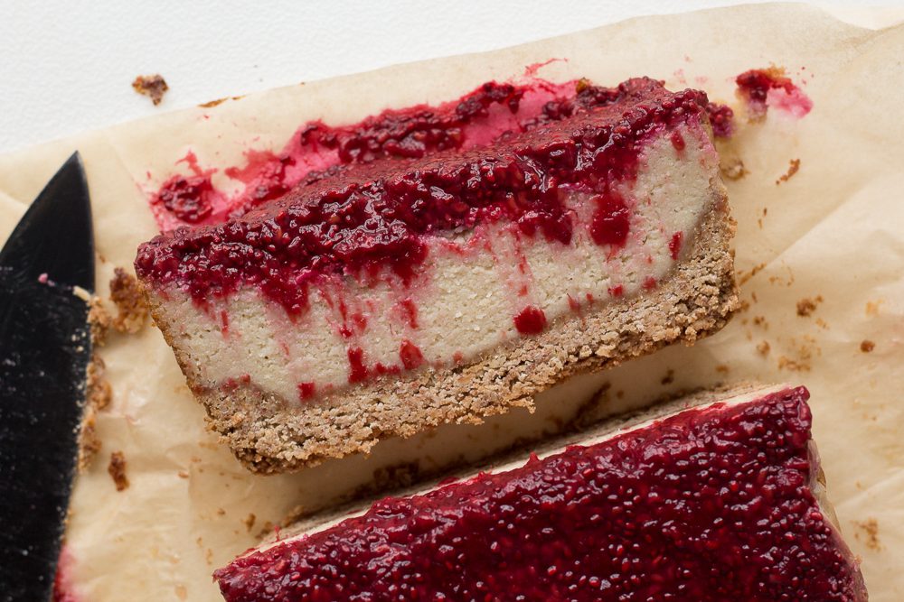 Vegan Raspberry Cheesecake sliced on parchment paper with a knife by Flora & Vino