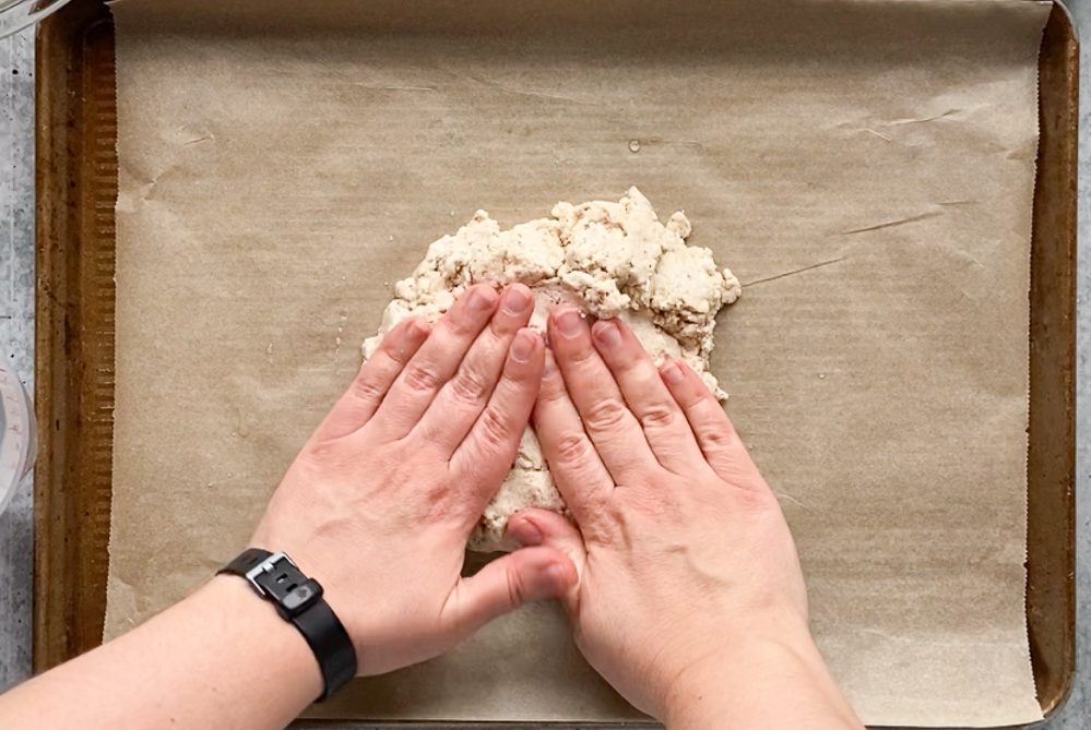 hands kneading flatbread pizza sough on parchment lined baking sheet