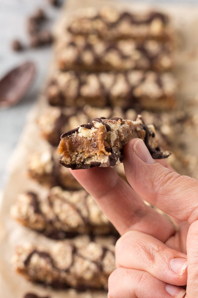 one Date Caramel Nougat Bars in hand with bite missing by Flora & Vino