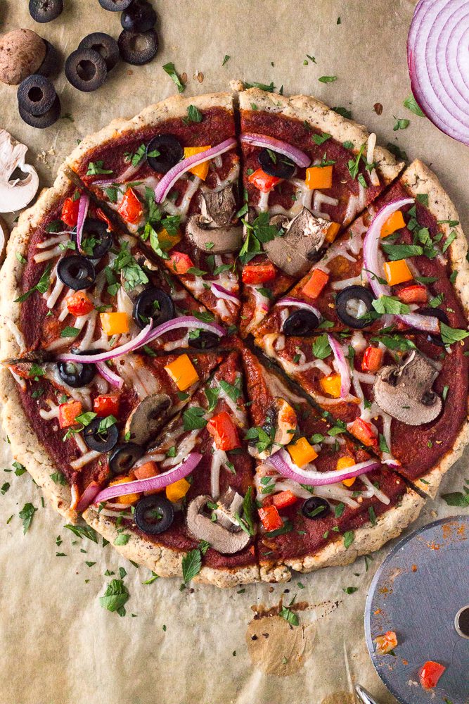 Veggie Lover's Flatbread Pizza served on parchment paper with pizza cutter, olives, mushrooms, and onion sprinkled with fresh herbs 