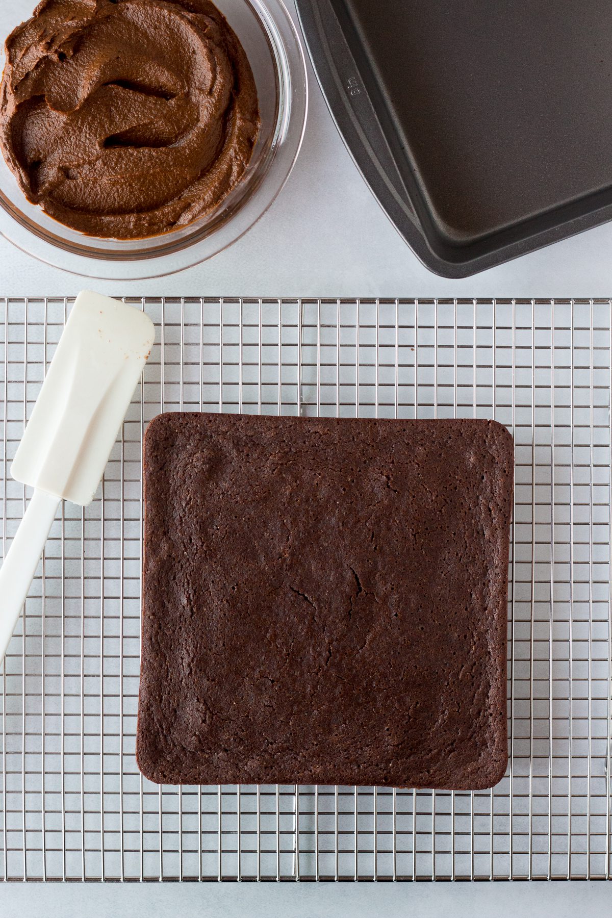 vegan chocolate cake on cooling rack with spatula and chocolate sweet potato frosting in bowl on the side 
