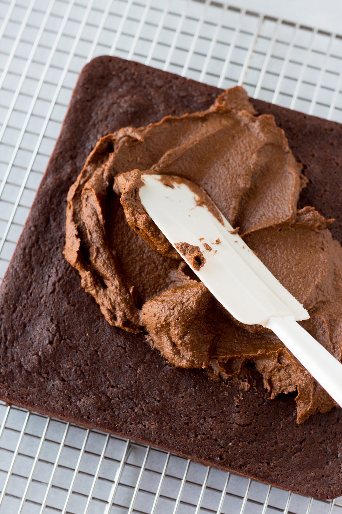 chocolate sweet potato frosting spread on vegan chocolate cake with spatula on cooling rack 
