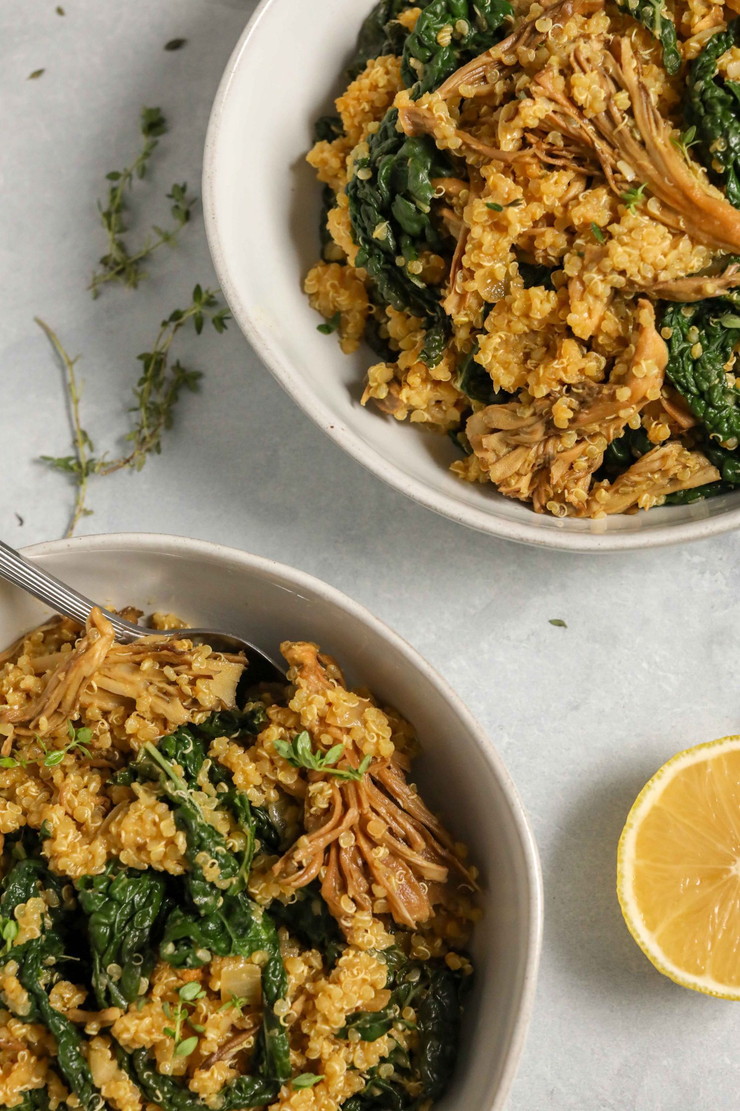 Kale Quinoa Mushroom Risotto served in bowl with lemon and scattered fresh thyme and spoons