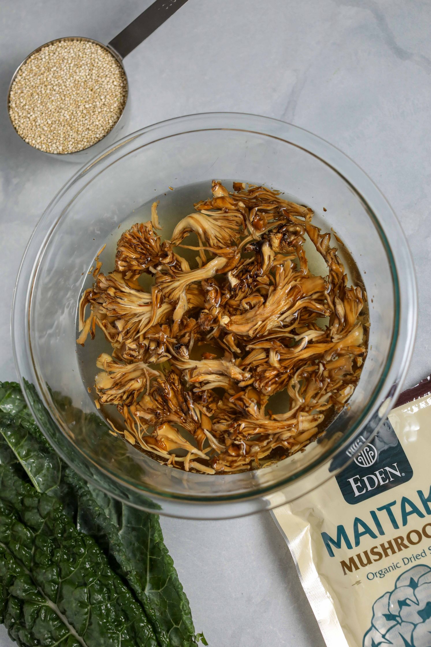 dried mushrooms soaking in water in glass bowl with quinoa and kale on the side