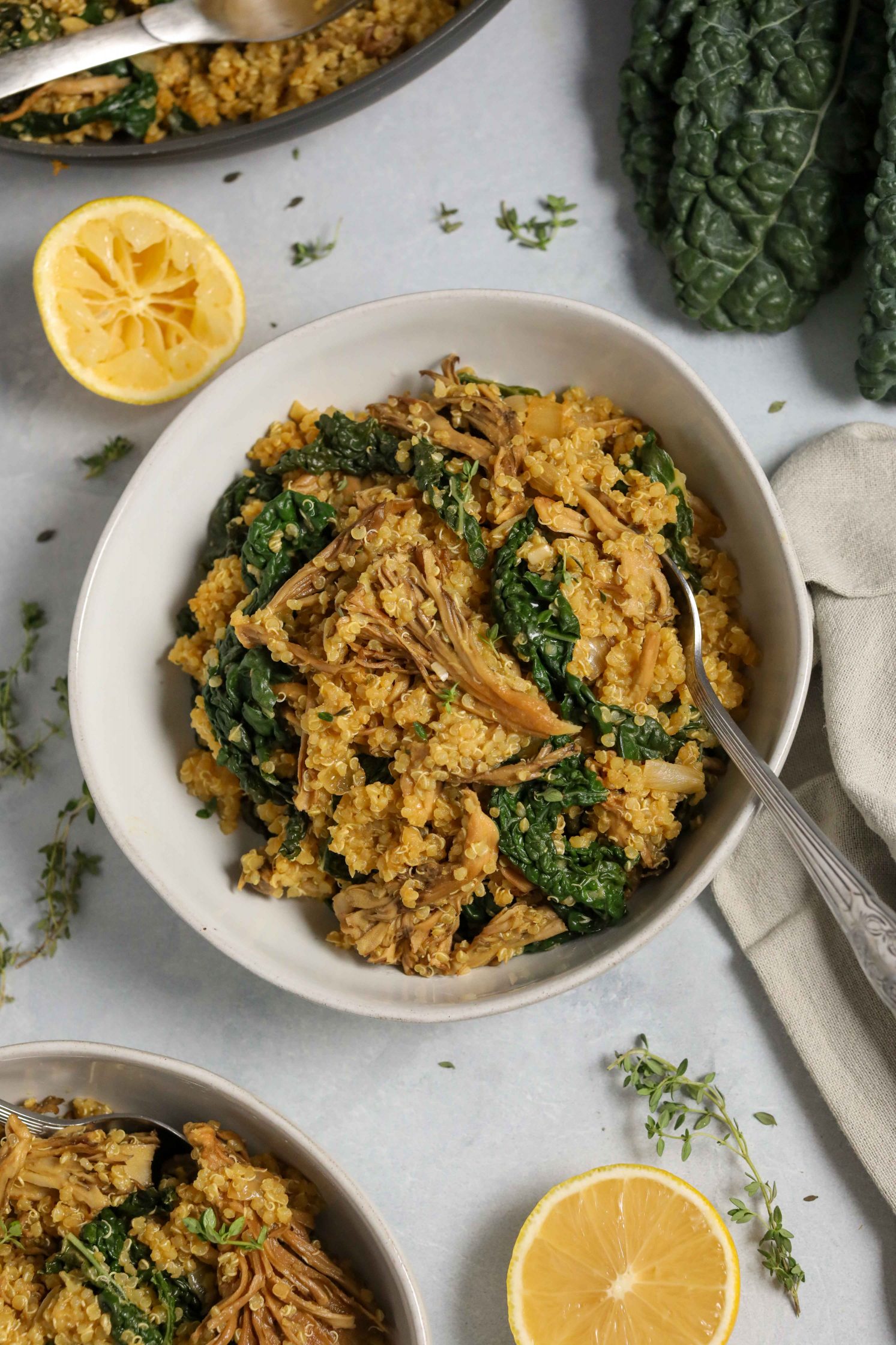 Kale Quinoa Mushroom Risotto served in bowl with lemon and scattered fresh thyme and spoons
