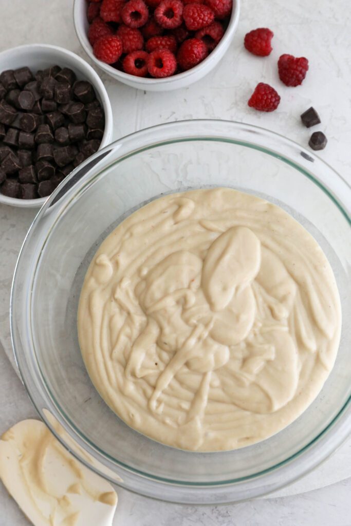 white bean blondie batter in glass bowl with raspberries and chocolate chips on the side by Flora & Vino