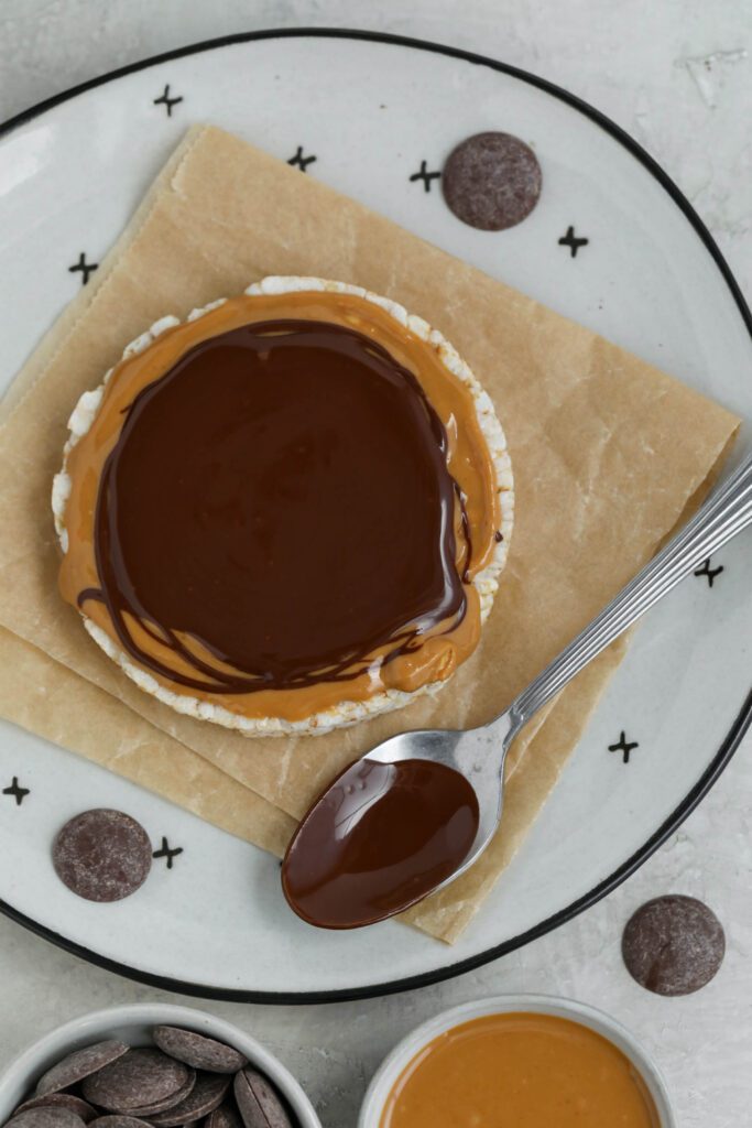 Chocolate Peanut Butter Rice Cake served on parchment paper lined plate with scattered cacao nibs, chocolate wafers, and peanut butter